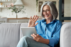 Happy 60s older mature middle aged adult woman waving hand holding digital tablet