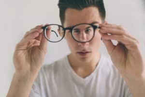 Handsome guy is holding his eyeglasses right in front of camera with one hand