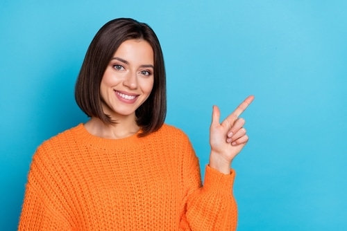 A cheerful girl in bright orange knitted sweater demonstrating a empty hand copy space sign